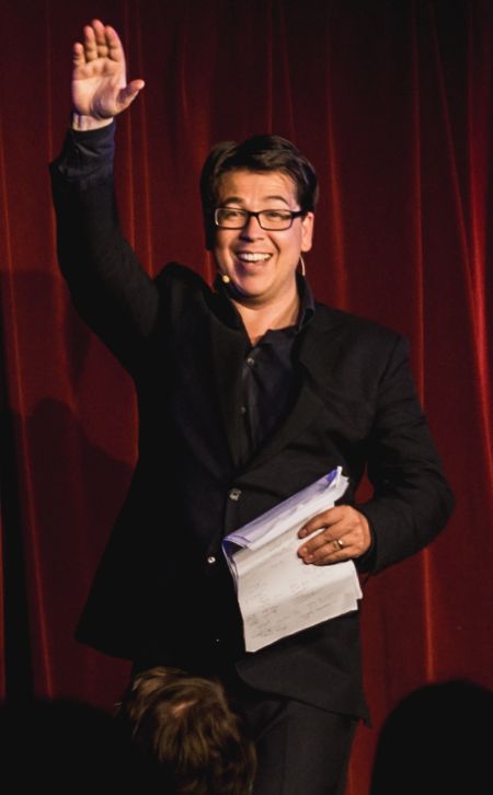 Michael McIntyre in a black suit poses at a comedy show.
